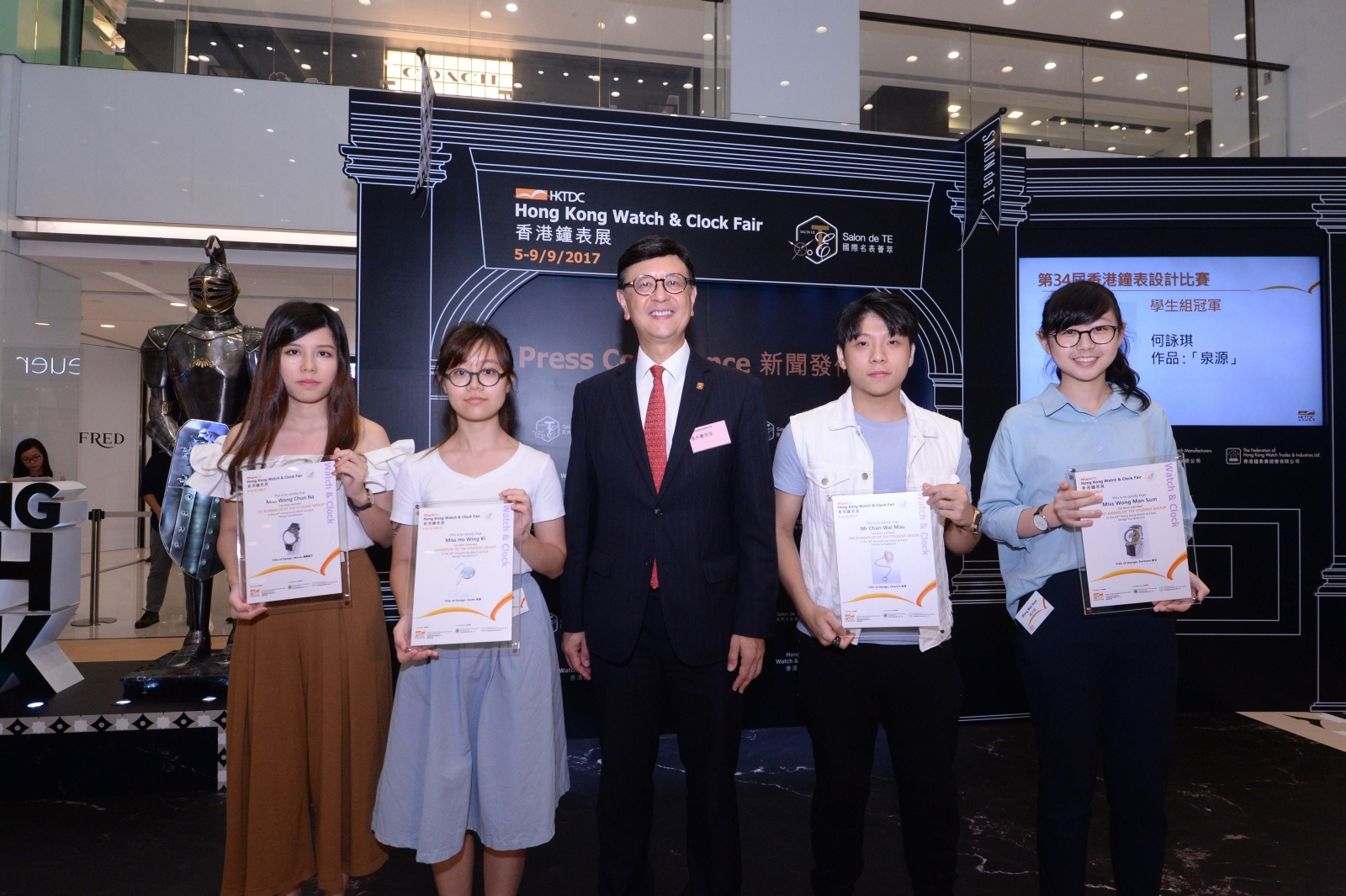 VTC students HO Wing-ki (second from left), WONG Chun-na (first from left), CHAN Wai-mau (second from right) and WONG Man-sum (first from right) sweep the championship, first and second runner-up prizes and merit award of the Student Group in the 34th Hong Kong Watch & Clock Design Competition. Together they receive the prizes from Chairman of the Federation of Hong Kong Watch Trades and Industries Ltd Harold SUN (centre). (Photo provided by HKTDC)